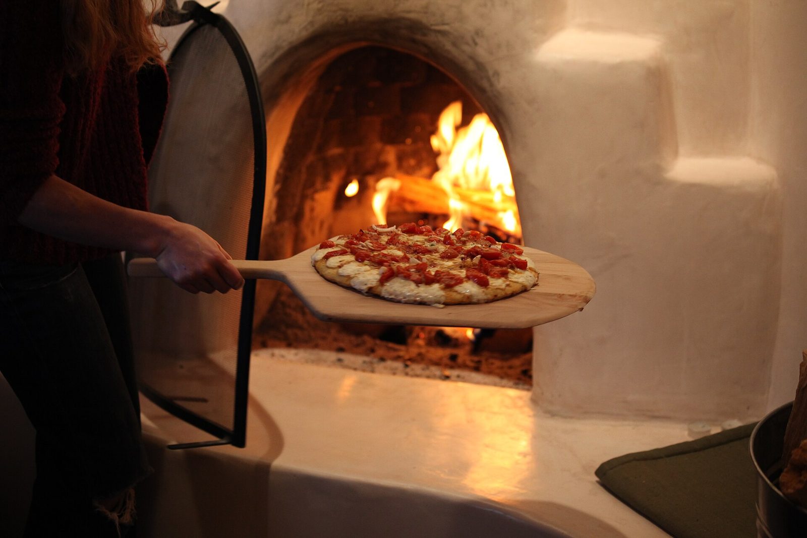 A wood-fired pizza coming out of a flaming oven on a wooden peel