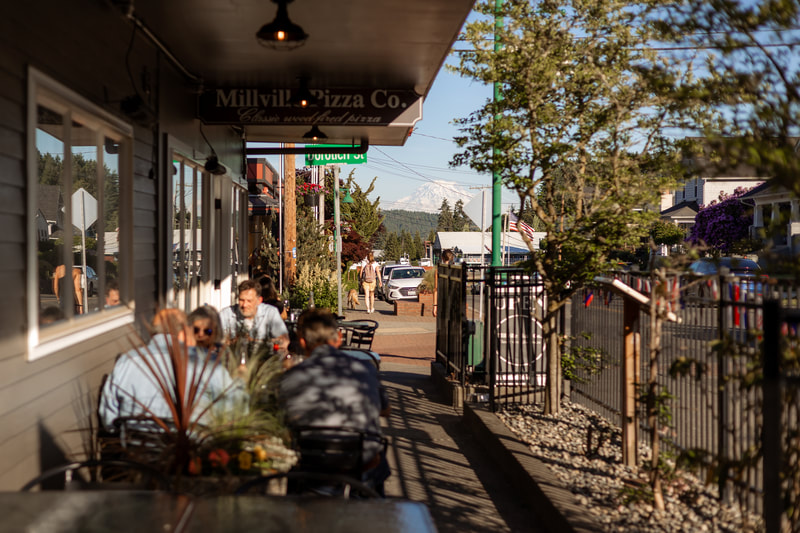 The Millville Pizza Co. storefront with diners on the patio and Mount Rainier in the distance
