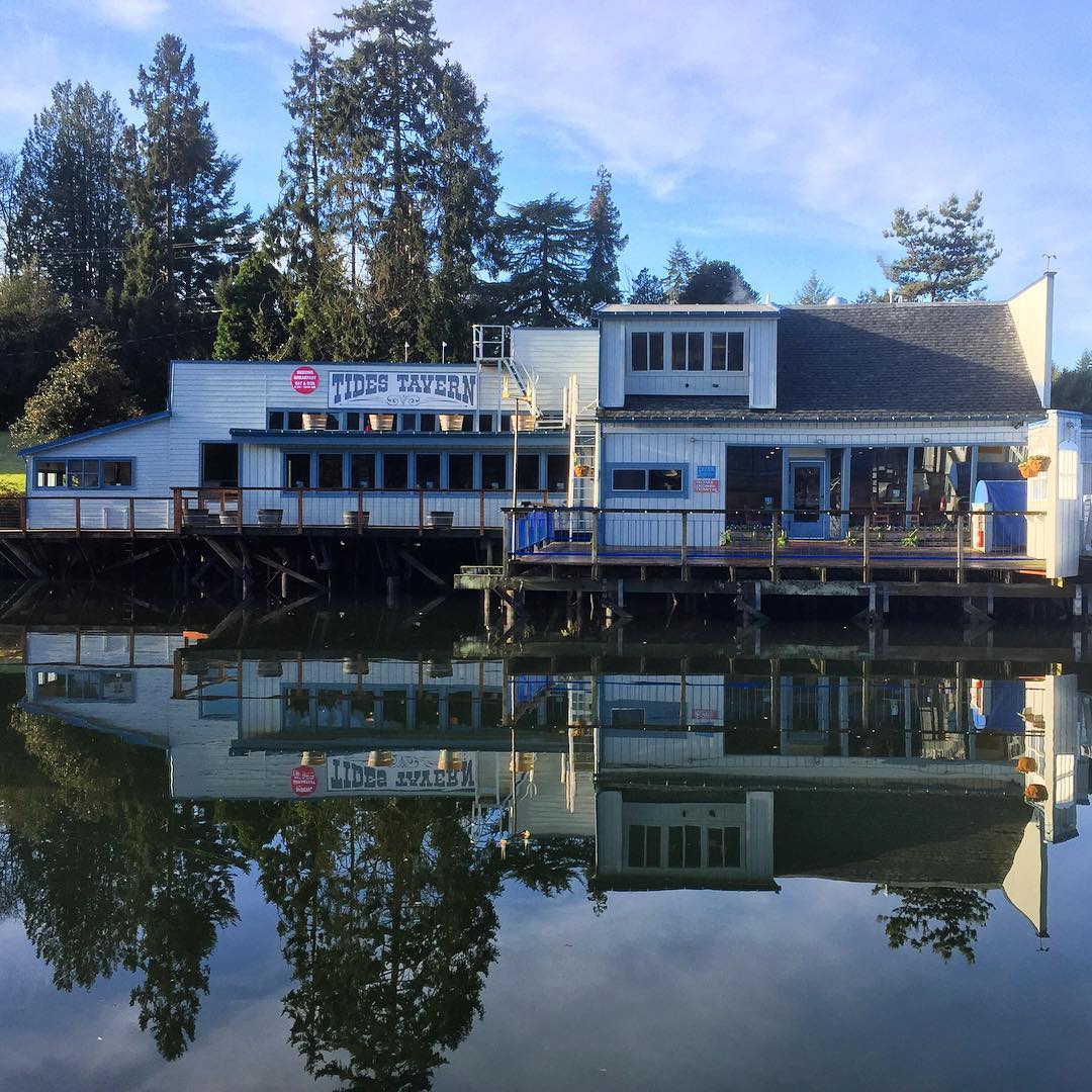 The Tides Tavern building over the water, reflected in the harbor, with its sign visible