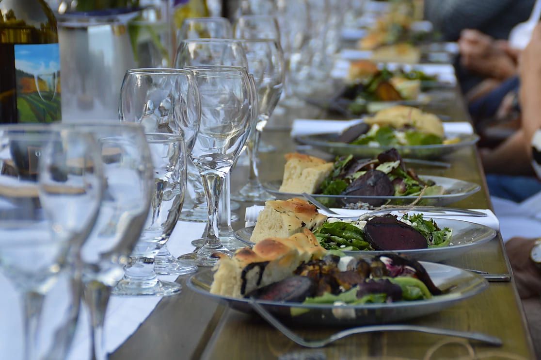 A long communal table set with wine glasses and plated salads at Dinner in the Vineyard, Olalla Vineyard and Winery