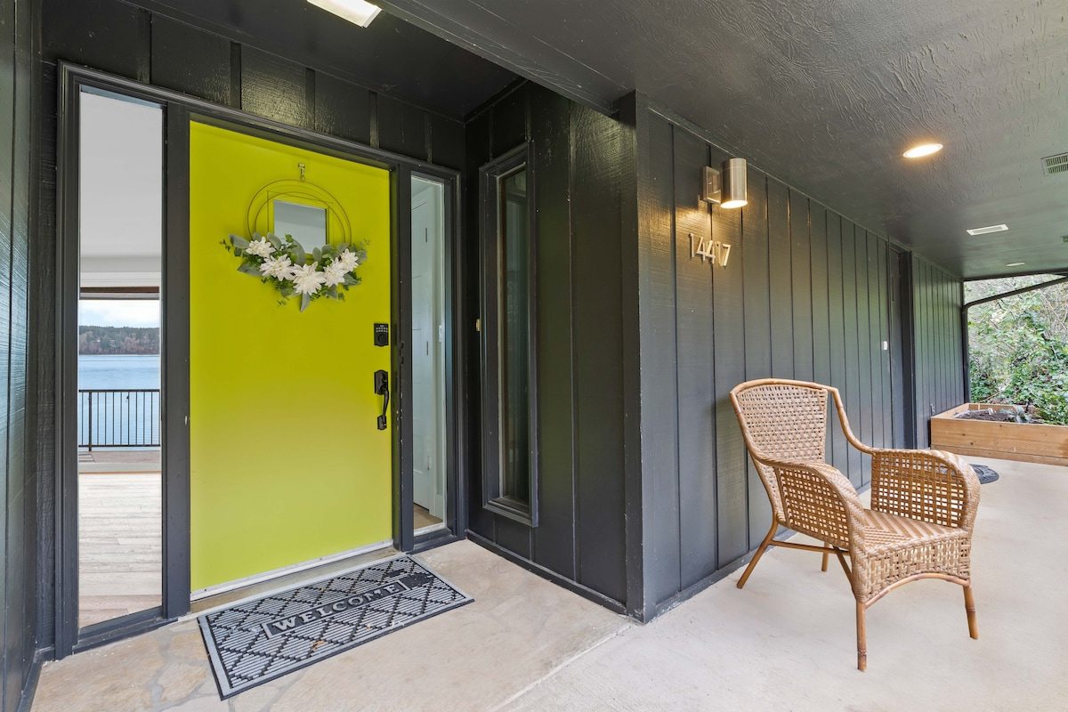The front entry today: chartreuse front door with wreath, dark siding, and wicker chair